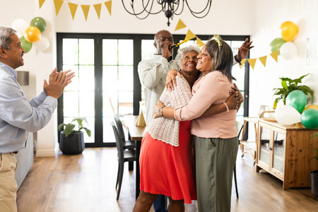 Elderly friends celebrating birthday at home, hugging and smiling with joy. Celebration, friendship, party, happiness, seniors, companionshipの写真素材