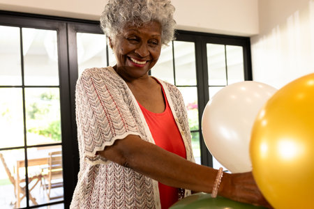 African American woman smiling while arranging colorful balloons at home celebration. Party, decoration, joy, happiness, festive, eventの写真素材
