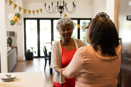 Celebrating birthday at home, African American women smiling and holding hands warmly. Celebration, happiness, community, friendship, togetherness, diversityの写真素材