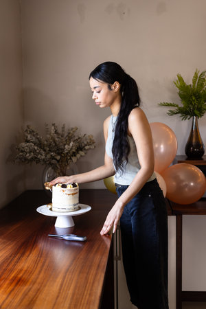Woman decorating cake with gold sprinkles at home, preparing for celebration. Baking, homemade,...