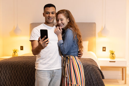 Young couple taking selfie together in cozy bedroom, smiling and enjoying moment. happiness, togetherness, lifestyleの写真素材