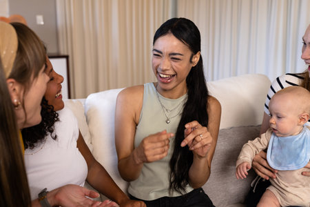 Friends laughing and bonding on couch while woman holds baby, enjoying time together. Friendship,...