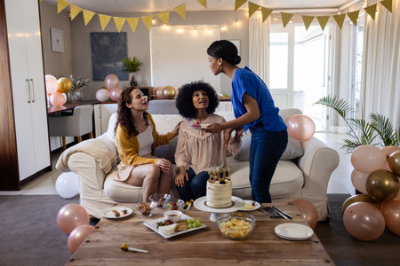 Friends celebrating birthday at home, enjoying cake and snacks with decorations. Celebration, party, friendship, food, indoors, gatheringの写真素材