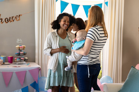 Celebrating baby shower, women holding baby and chatting in living room, smiling. Celebration, motherhood, family, gathering, friendship, partyの写真素材