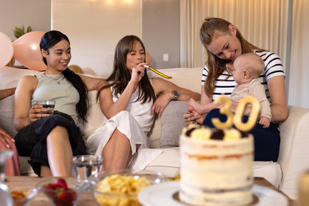 Celebrating birthday, women enjoying party with cake and baby on cozy sofa. Celebration, family,...