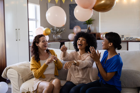 Women laughing and celebrating with balloons at home, enjoying festive atmosphere. Celebration, happiness, festivity, friendship, cheerful, gatheringの写真素材