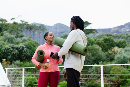 African American friends in gym gear standing by railing on balcony holding yoga mats, smartphone. Outdoor, wellness, fitness, casual, nature, tranquility, inspirationの写真素材