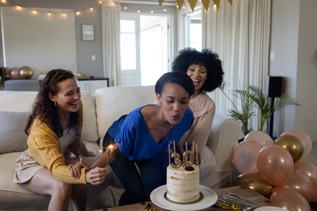 Celebrating birthday, woman blowing candles on cake with friends at home. celebration, party, happiness, gatheringの写真素材