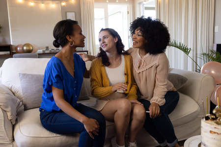 Three women sitting on sofa celebrating birthday with cake and balloons at home. Celebration, party,...