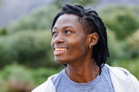 African American man smiling and standing in park wearing hoodie and hoop earring, copy space. Nature, outdoor, casual, portrait, wellness, serenity, lifestyleの写真素材