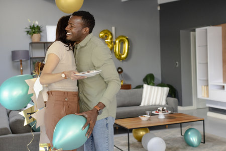 Friends hugging and celebrating birthday with balloons and cake at home. Celebration, friendship, party, happiness, fun, joyの写真素材