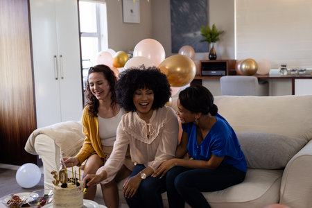 Celebrating at home, three women laughing and enjoying cake with balloons around. Celebration, happiness, friendship, party, dessert, festiveの写真素材
