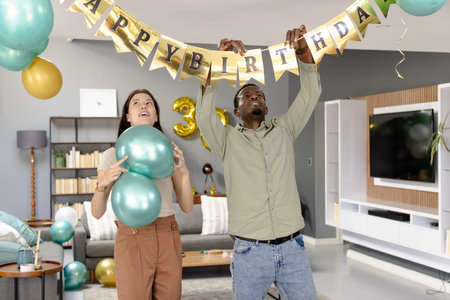 Preparing living room for celebration, friends decorating with birthday banner. party, decorations, gathering, friendship, festive, joyfulの写真素材