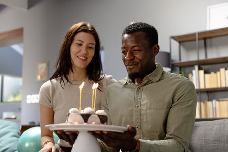 Celebrating birthday, couple smiling with cake and candles at home. Celebration, happiness, indoors,...