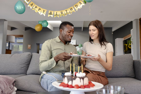Celebrating birthday, couple enjoying cake together on living room sofa. Party, celebration, happiness, romance, cozy, sweetsの写真素材