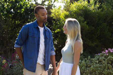 Couple enjoying romantic moment in garden, holding hands and smiling warmly. Romance, affection, love, happiness, relationship, togethernessの写真素材