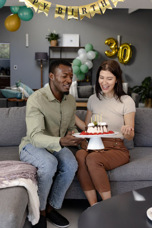 Celebrating birthday, couple sharing cake on sofa with joyful expressions. Celebration, happiness, partners, dessert, event, togetherの写真素材