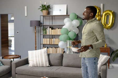 African American man holding snacks and drink, celebrating birthday at home. Celebration, party, food, happiness, festive, enjoymentの写真素材