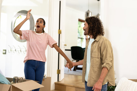Young diverse couple unpacking moving boxes, feeling excited and joyful in new home. Relocation, happiness, settling, beginning, familyの写真素材