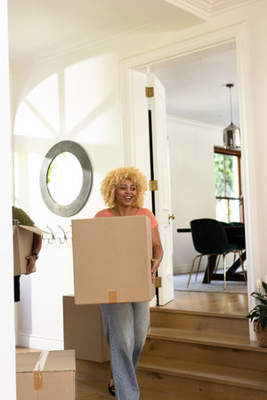 Young woman carrying moving boxes into new home, smiling with excitement. Relocation, unpacking,...