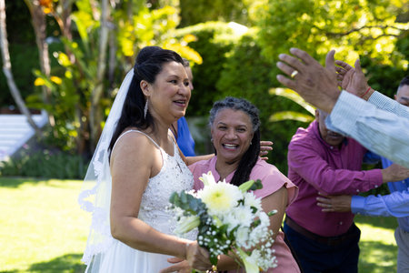 Bride celebrating with friends in garden, holding bouquet and smiling joyfully. senior wedding, celebration, bridal, friendship, happiness, outdoorの写真素材