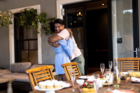 Diverse friends hugging joyfully at outdoor gathering with cupcakes and champagne on table. Celebration, friendship, bonding, outdoors, party, togethernessの写真素材