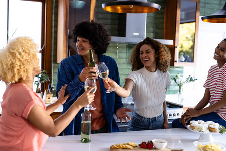 Diverse friends toasting with drinks in modern kitchen, enjoying celebration together. Party, friendship, gathering, beverage, socializing, indoorsの写真素材