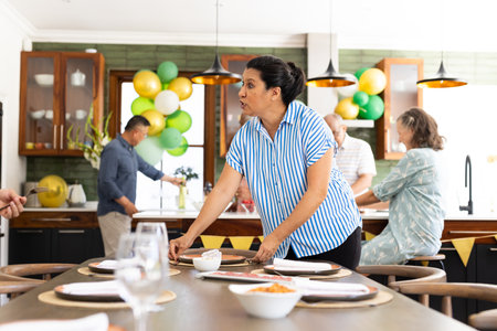 In kitchen, family arranging table and preparing for celebration, chatting happily. preparation, party, cooking, festivityの写真素材