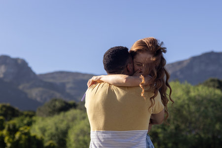 Young couple embracing outdoors with mountains in background, sharing joyful moment. Love, nature, happiness, romance, adventure, scenicの写真素材