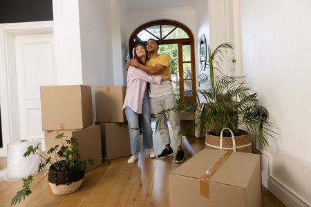 Young couple embracing in new home surrounded by moving boxes and plants. unpacking, relocation,...