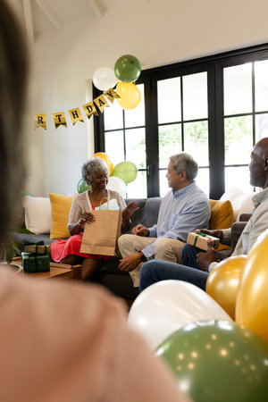 Opening gifts with family, elderly woman celebrating birthday joyfully at home. Celebration, family time, happiness, togetherness, presents, cheerfulの写真素材