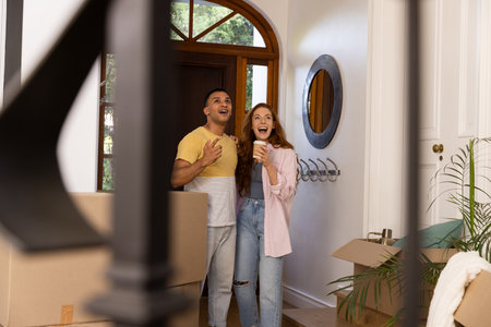 Young couple excitedly entering new home surrounded by moving boxes and plants. Homeownership,...