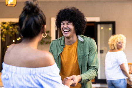 Young man laughing and holding hands with woman at outdoor gathering. Diverse friends, social, bonding, happiness, enjoyment, celebrationの写真素材