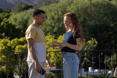 Holding smartphone and conversing, couple outdoors surrounded by nature. technology, communication, togetherness, greeneryの写真素材