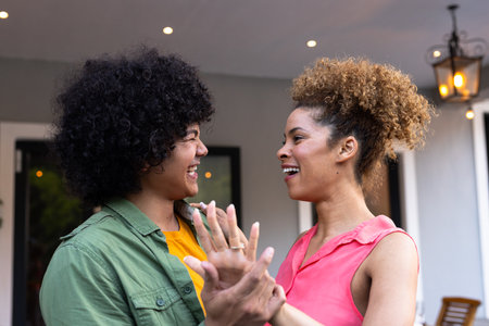 Two young women laughing and holding hands, enjoying joyful moment together. Friendship, happiness, bonding, laughter, togetherness, outdoorsの写真素材
