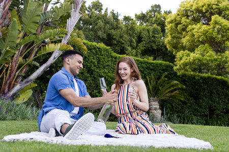 Young couple enjoying picnic outdoors, sharing champagne and smiling on blanket. romance,...