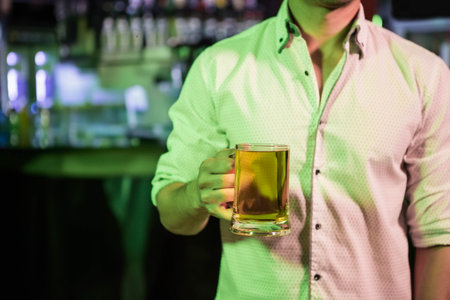 Beer mug resting on bar counter under greenish ambient lighting with blurred liquor bottles. Nightlife, leisure, socializing, modern, vibrant, casual, atmosphereの写真素材