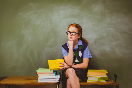 Girl student sitting on bench in classroom holding yellow book amid book stacks and chalkboard. Educational, learning, academic, scholastic, youth, literacy, classroomの写真素材