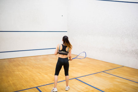 Squash player preparing to swing racket at ball on wooden court, blue lines and scuff marks. Athlete, fitness, sport, training, agility, competition, modernの写真素材