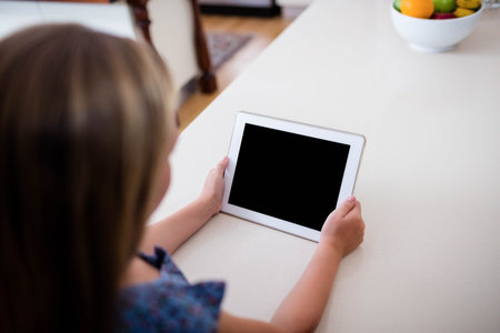 Female child sitting on home kitchen countertop holding white tablet near colorful fruit bowl. Child, technology, lifestyle, minimalist, family, education, wellnessの写真素材