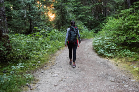 Female hiker walking along dirt trail wearing gray top, leggings and hiking shoes carrying backpack....