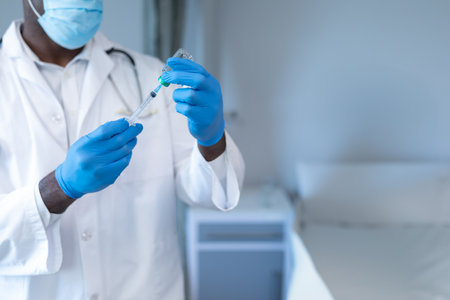 African American male doctor drawing medication from vial into syringe in clinic, copy space. Medical, healthcare, clinical, laboratory, professional, treatment, sanitationの写真素材