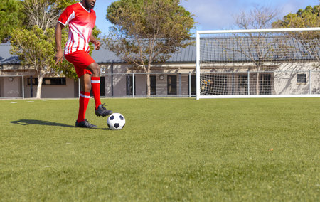 African American man controlling soccer ball near goalpost on turf in red uniform, copy space. Athlete, sports, athleticism, training, playground, outdoor, activityの写真素材