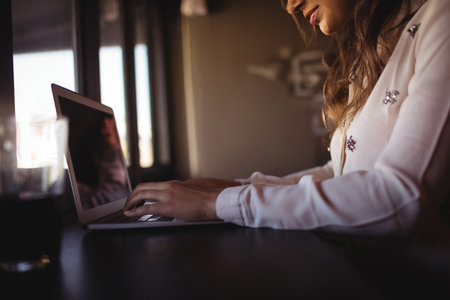 Woman typing on laptop at wooden table by window blinds with glass of water, copy space. Minimalist, professional, cozy, workspace, ambient, serene, modernの写真素材