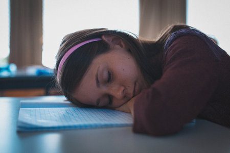 Female child resting head on open lined notebook at desk in classroom wearing pink headband. Youth, education, study, concentration, tranquil, morning, learningの写真素材