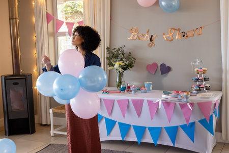 African American woman holding pastel balloons, decorating dining area for baby shower, copy space. Celebration, femininity, elegance, festive, hospitality, joy, domesticの写真素材
