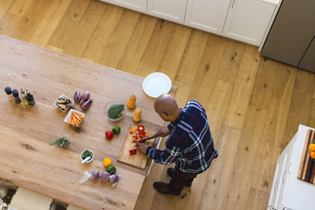 African American senior male chopping red bell peppers on wooden table in home kitchen, copy space....
