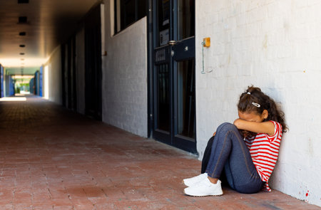 Girl child sitting on red brick corridor floor in covered hallway wearing striped shirt, copy space. Urban, architecture, minimalism, solitude, relax, contemplative, corridorの写真素材