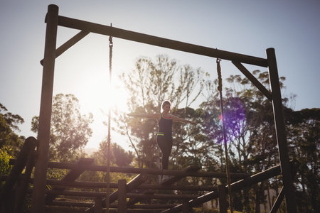 Woman balancing on horizontal wooden beam on forest obstacle course, sun creating lens flare. Adventure, fitness, resilience, outdooractivity, athleticism, endurance, naturalの写真素材