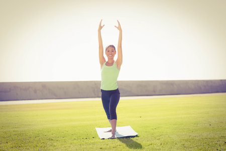 Female in green sportswear performing yoga on white yoga mat on grassy lawn under bright sky. Outdoor, wellness, mindfulness, nature, serenity, fitness, tranquilityの写真素材